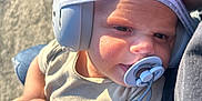 Felix is registered to the contest to win money with this photo: baby, headphones, pacifier, infant, child, closeup, outdoor, sunlight, person, clothing, adult_arm, hair, cute, holding, accessory, beige_shirt, blue_jeans, blurred_background, texture, casual