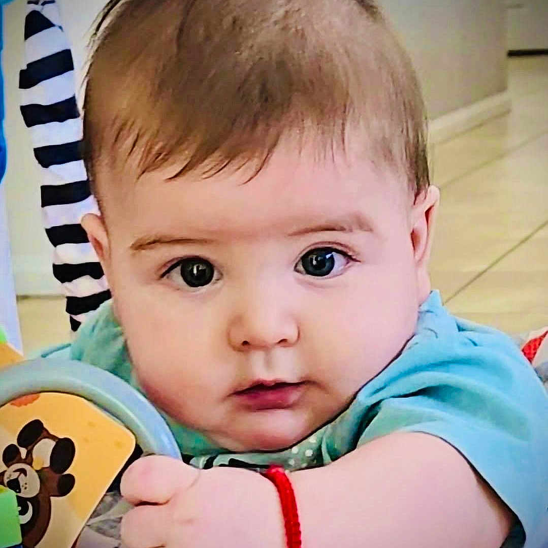 Alessandro is registered to the contest to win money with this photo: baby, blue_shirt, bracelet, child, closeup, colorful, curious, cute, expression, face, floor, hand, home, indoor, infant, person, playful, striped_background, toy, young