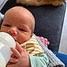 baby, bottle, feeding, hands, adult, knitted_sleeve, couch, cat_tail, orange_cat, indoor, closeup, portrait, newborn, striped_bib, holding, comfort, cozy, human, resting, casual