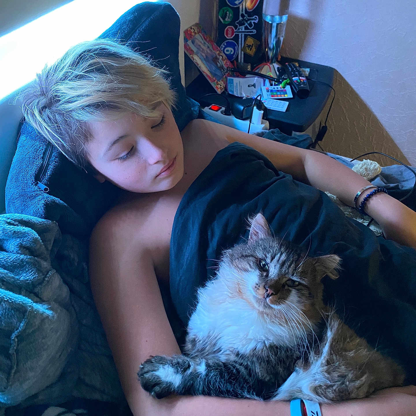 Mousquetaire participe au concours pour gagner de l'argent avec cette photo : person, cat, bed, blanket, resting, sleepy, indoor, window_light, bracelet, nightstand, remote_control, lamp, hair, furniture, sleep, relaxing, cozy, fur, comfort, home