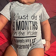 Kingston is registered to the contest to win money with this photo: baby, infant, child, onesie, gray_clothing, lying_down, blanket, patterned_blanket, text_on_clothing, cute, young_child, human, portrait, indoors, skin, legs, arms, expression, soft_lighting, casual