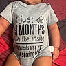 baby, infant, child, onesie, gray_clothing, lying_down, blanket, patterned_blanket, text_on_clothing, cute, young_child, human, portrait, indoors, skin, legs, arms, expression, soft_lighting, casual