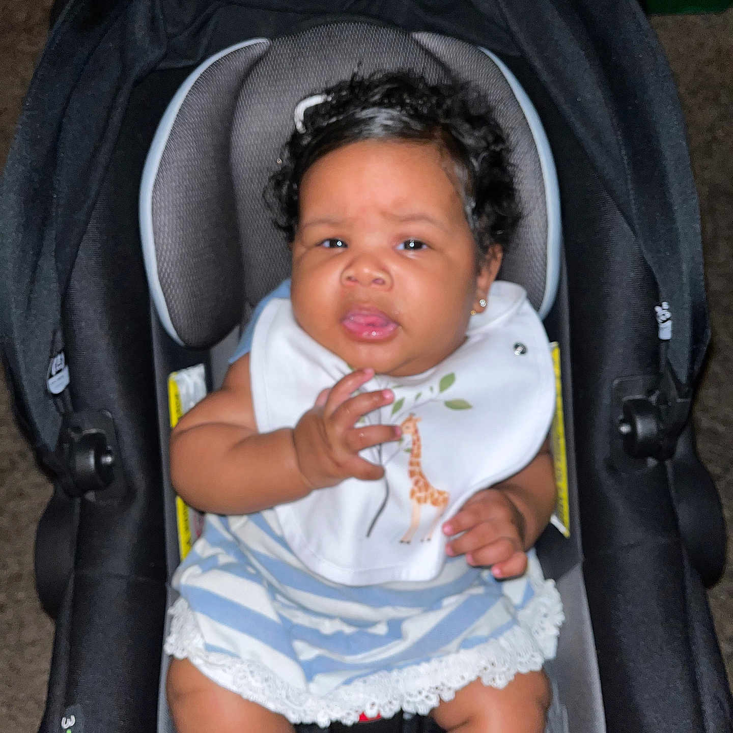 Erinét joined the competition — help win amazing prizes! baby, bib, car, car_seat, child, clothing, curly_hair, cute, ears, expression, fabric, face, hand, indoor, infant, person, safety, seatbelt, sitting, striped_dress