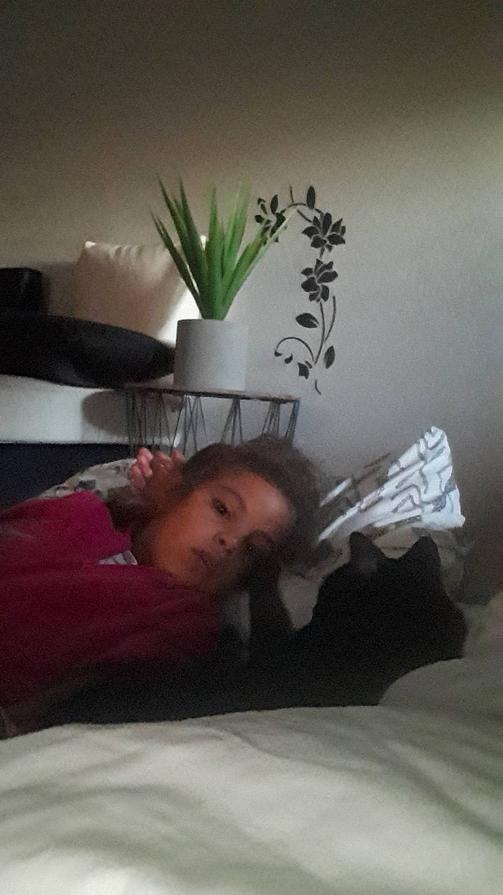 Inès participe au concours pour gagner de l'argent avec cette photo : bed, bed_sheet, bedding, bedroom, comfort, floor, flooring, furniture, gesture, hardwood, human_leg, interior_design, lighting, linens, person, pillow, plant, room, sitting, throw_pillow