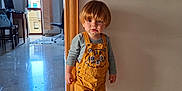 Martin participe au concours pour gagner de l'argent avec cette photo : toddler, child, indoor, yellow_overalls, standing, curly_hair, doorframe, marble_floor, home_office, lamp, chair, window, reflection, long_sleeve_shirt, shoes, wall, floor, person, casual_clothing, portrait