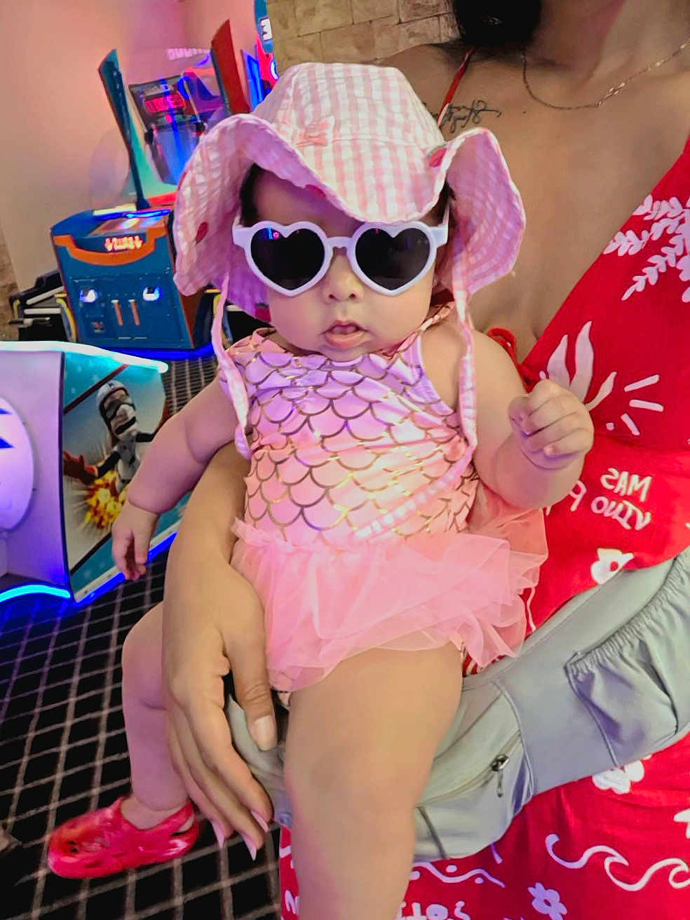 Marbella Esparza is registered to the contest to win money with this photo: baby, child, sunglasses, hat, pink, dress, tutu, hand, adult, arcade, gaming_machine, floor, pattern, person, indoor, fashion, accessory, red_dress, holding, cute