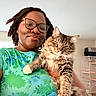 person, cat, glasses, indoor, floral_shirt, tabby_cat, white_paws, smile, holding, pet, feline, portrait, happy, animal, cozy, natural_light, home, cute, friendly, closeup