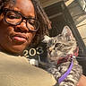 person, cat, kitten, glasses, bow_tie, leash, outdoor, sunlight, portrait, face, hair, building, door, number, animal, pet, feline, closeup, expression, home