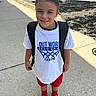 child, smiling, outdoor, sidewalk, tshirt, backpack, red_shorts, red_socks, brown_slippers, person, daylight, parking_lot, bench, car, concrete, shadow, hair_tied_back, casual_clothing, young, happy