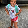 child, smiling, outdoor, tshirt, shorts, backpack, person, standing, confident_pose, gravel, vehicle, footwear, happy, casual_clothing, young, summer, cute, playful, portrait, fashion