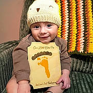Maclaine is registered to the contest to win money with this photo: baby, infant, child, hat, knitted_hat, plaque, footprint, thanksgiving, smile, sitting, couch, blanket, crocheted_blanket, hand, face, cute, indoors, cozy, holiday, portrait