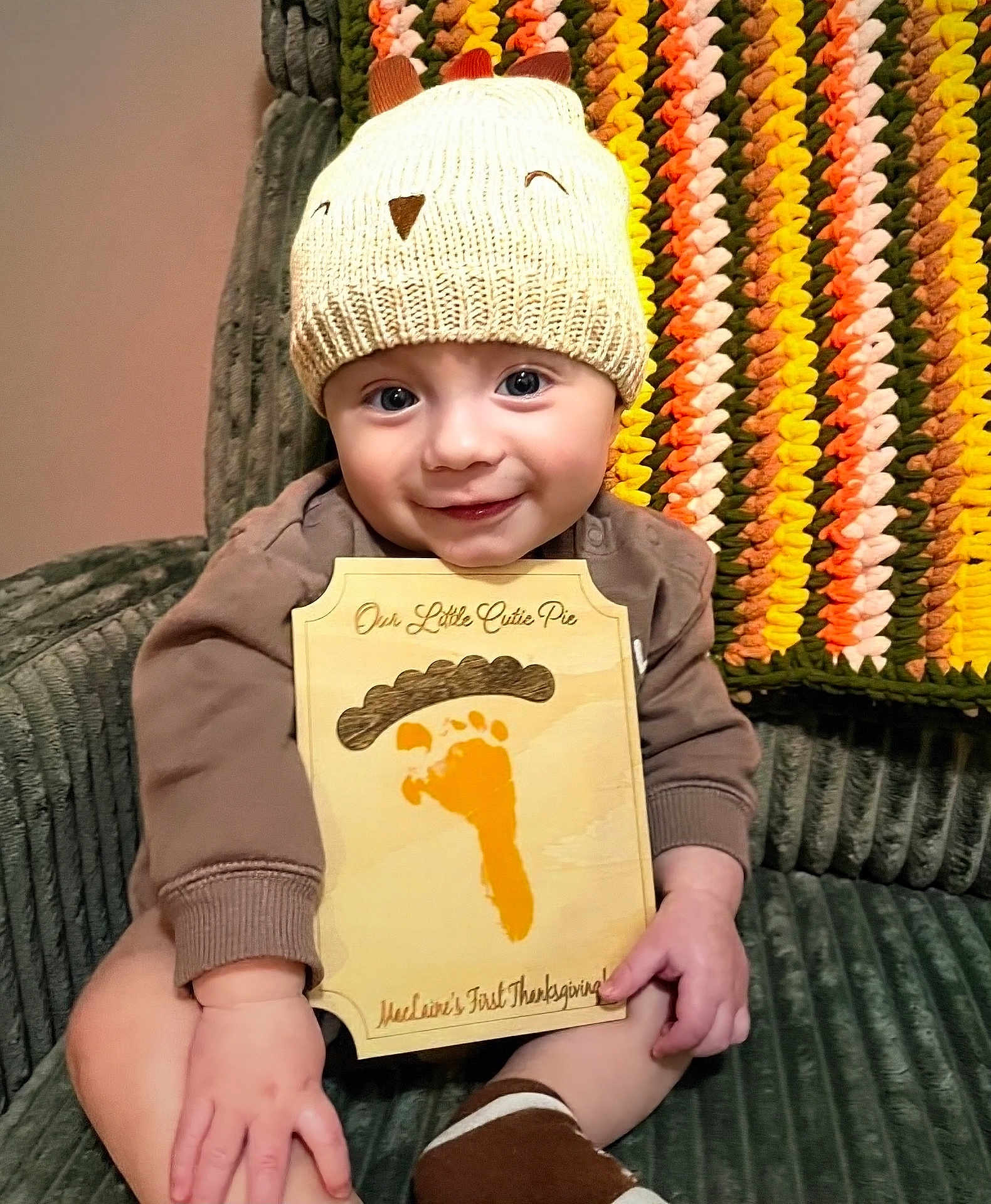 Maclaine is registered to the contest to win money with this photo: baby, infant, child, hat, knitted_hat, plaque, footprint, thanksgiving, smile, sitting, couch, blanket, crocheted_blanket, hand, face, cute, indoors, cozy, holiday, portrait