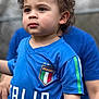 toddler, child, curly_hair, blue_jersey, italia, soccer, sportswear, portrait, outdoor, person, face, expression, closeup, casual_clothing, young_child, short_sleeves, focused, background_blur, daylight, human