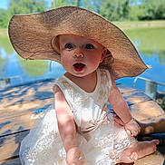 Maïa participe au concours pour gagner de l'argent avec cette photo : baby, barefoot, bow, child, cute, dress, expression, hat, lace, lake, nature, outdoor, portrait, sitting, summer, sunhat, sunlight, trees, water, wooden_table