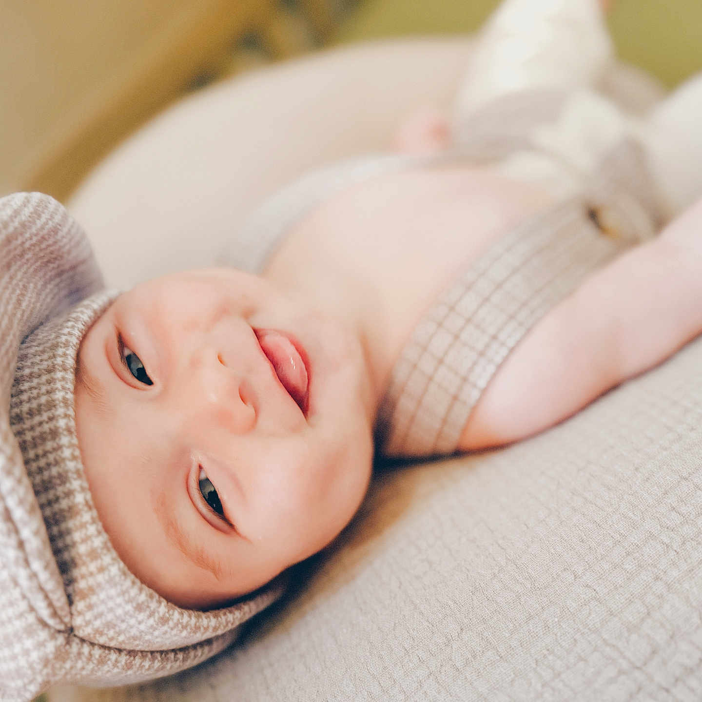 Emmett is registered to the contest to win money with this photo: apparel, baby, blanket, child, closeup, cute, expression, face, happy, hat, headwear, indoors, infant, lying_down, person, skin, smiling, soft_texture, tongue_out, warm_colors