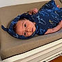 baby, infant, blue_clothing, shark_pattern, lying_down, changing_pad, bedroom, curious, face, child, cute, apparel, soft_texture, indoor, person, newborn, sleepwear, head, skin, expression