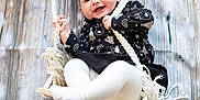 Ariana And Clara is registered to the contest to win money with this photo: baby, child, swing, smiling, black_dress, white_tights, rope, wooden_background, happy, cute, indoor, infant, holding, playful, portrait, person, clothing, seat, young_child, fun