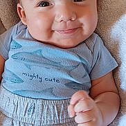 Alejandro is registered to the contest to win money with this photo: baby, smiling, blue_shirt, shorts, sharks, towel, cushion, cheeks, face, eyes, skin, clothing, infant, person, cute, hand, lying_down, indoors, soft_texture, happy