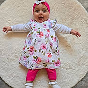 Maïa participe au concours pour gagner de l'argent avec cette photo : baby, infant, child, smiling, headband, bow, floral_dress, pink_leggings, white_socks, rug, floor, happy, lying_down, indoors, cute, portrait, person, clothing, fashion, baby_girl