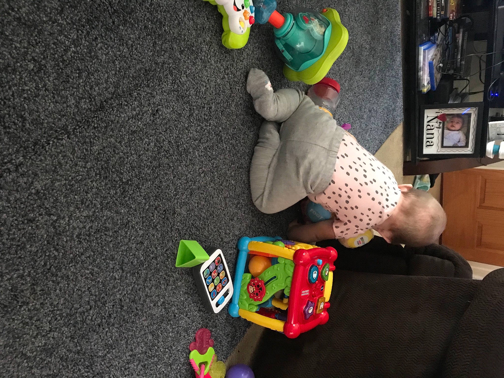 Adrianna is registered to the contest to win money with this photo: baby_toys, bookcase, cabinetry, child, fictional_character, fun, gadget, games, lap, person, play, plush, room, shelf, shelving, sitting, stuffed_toy, t_shirt, television, toy