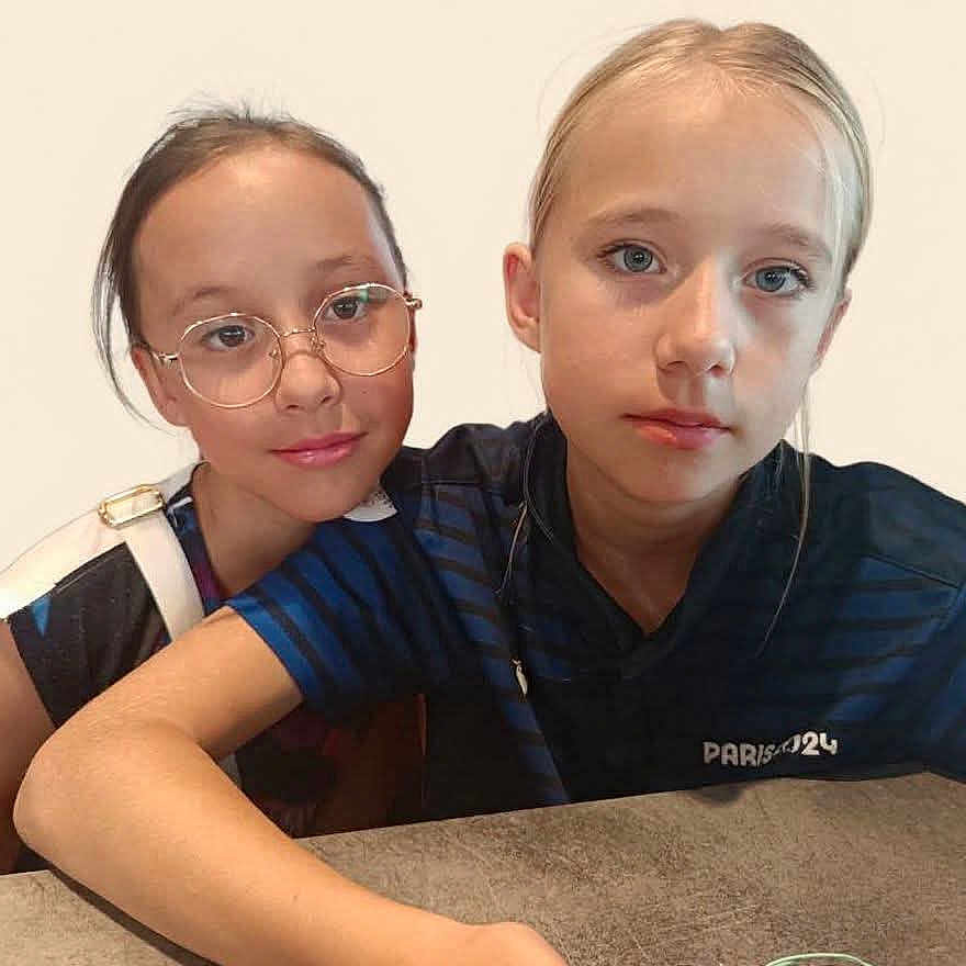 Fiona Lea a rejoint le concours — aidez-le/la à gagner de superbes lots ! blue_shirt, casual, child, children, expression, face, friendship, girl, glasses, hair, indoor, light_background, person, portrait, serious, shoulder, sitting, smile, table, young