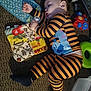 toddler, sleeping, pajamas, striped_clothing, pacifier, toy, book, carpet, indoor, child, baby, naptime, clothing, person, floor, relaxation, cute, rest, home, infant