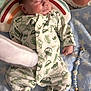 baby, sleeping, onesie, car_pattern, pillow, rainbow, blanket, star_pattern, pacifier, beaded_holder, toy, infant, cute, soft, cozy, hand, face, peaceful, indoors, resting