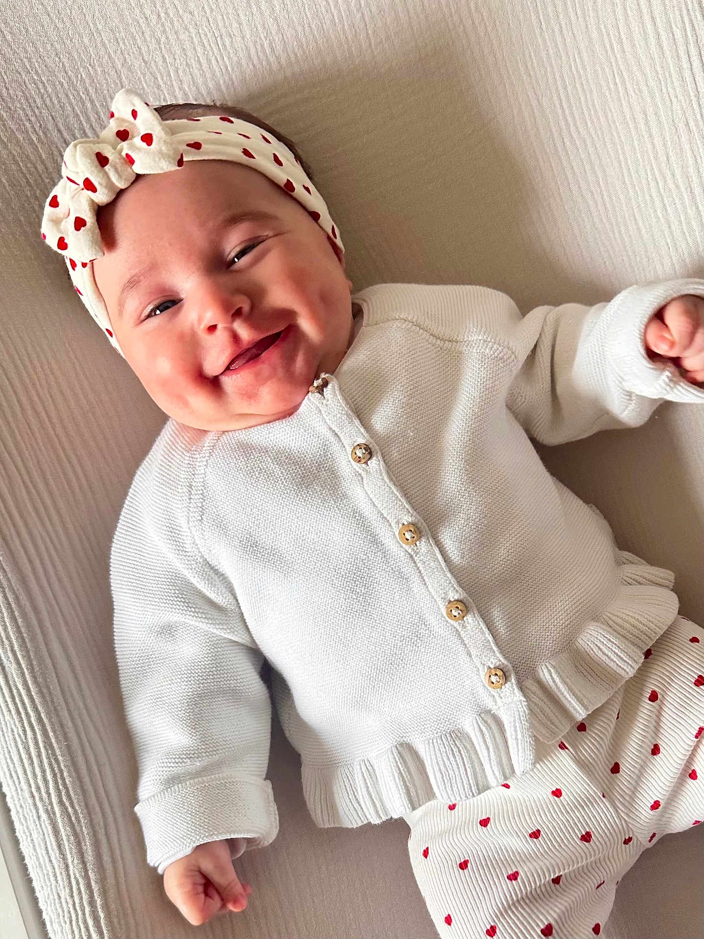 Ellie a rejoint le concours — aidez-le/la à gagner de superbes lots ! baby, infant, smile, headband, bow, white_cardigan, heart_pattern, pants, cute, cozy, closeup, portrait, child, happy, indoors, soft_lighting, neutral_background, clothing, apparel, resting