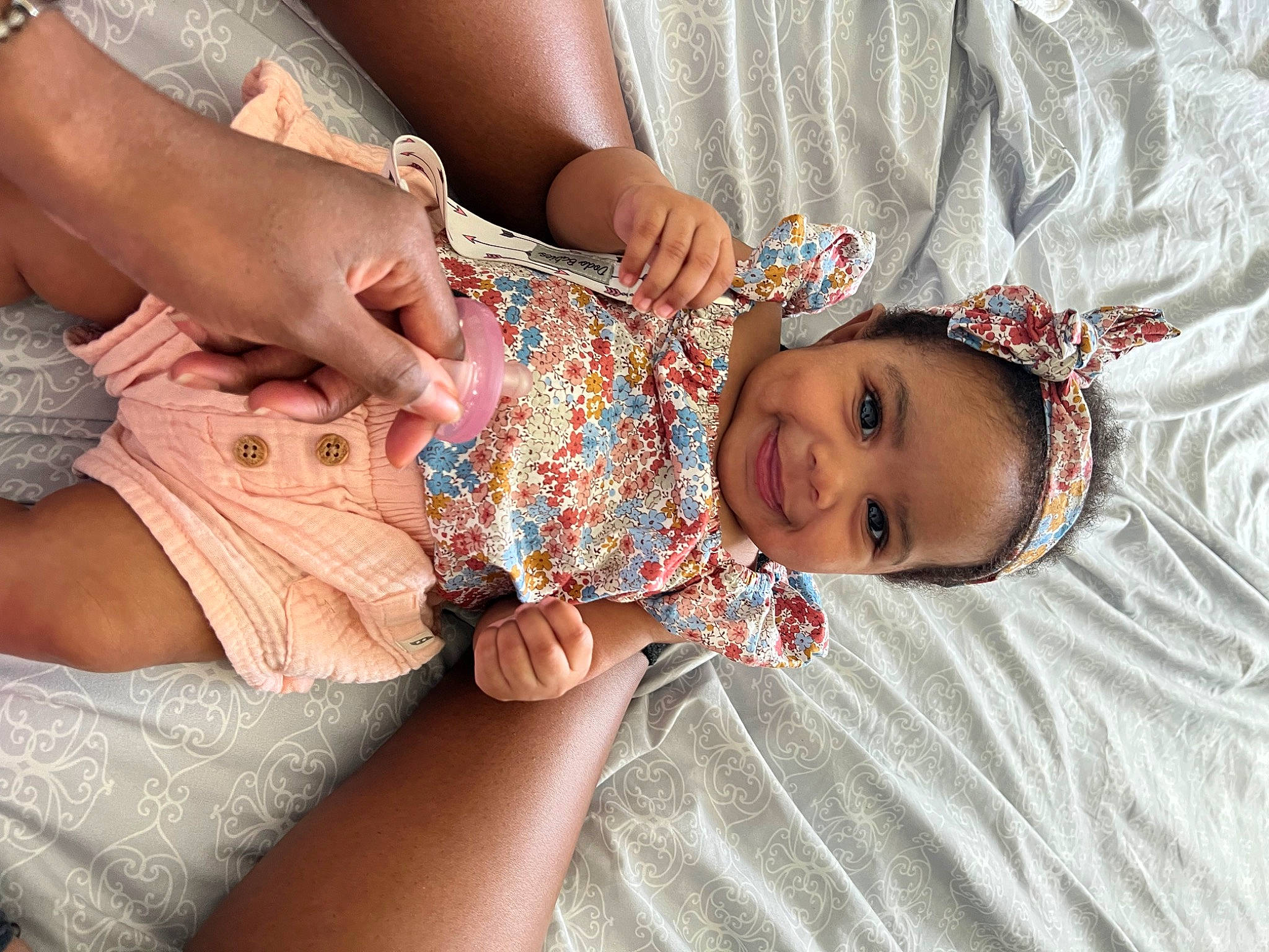 Nylah is registered to the contest to win money with this photo: baby, baby_toddler_clothing, child, comfort, dress, finger, fun, gesture, hand, happy, human_body, joy, nail, pattern, person, pink, skin, smile, textile, thumb