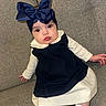 baby, infant, child, couch, sofa, headband, bow, clothing, dress, white, navy_blue, sitting, indoors, portrait, cute, face, person, sock, comfortable, expression