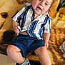 baby, child, smiling, blue_shoes, striped_shirt, shorts, blanket, indoor, happy, cute, footwear, patterned_blanket, infant, person, young_child, casual_clothing, sitting, legs, head, face