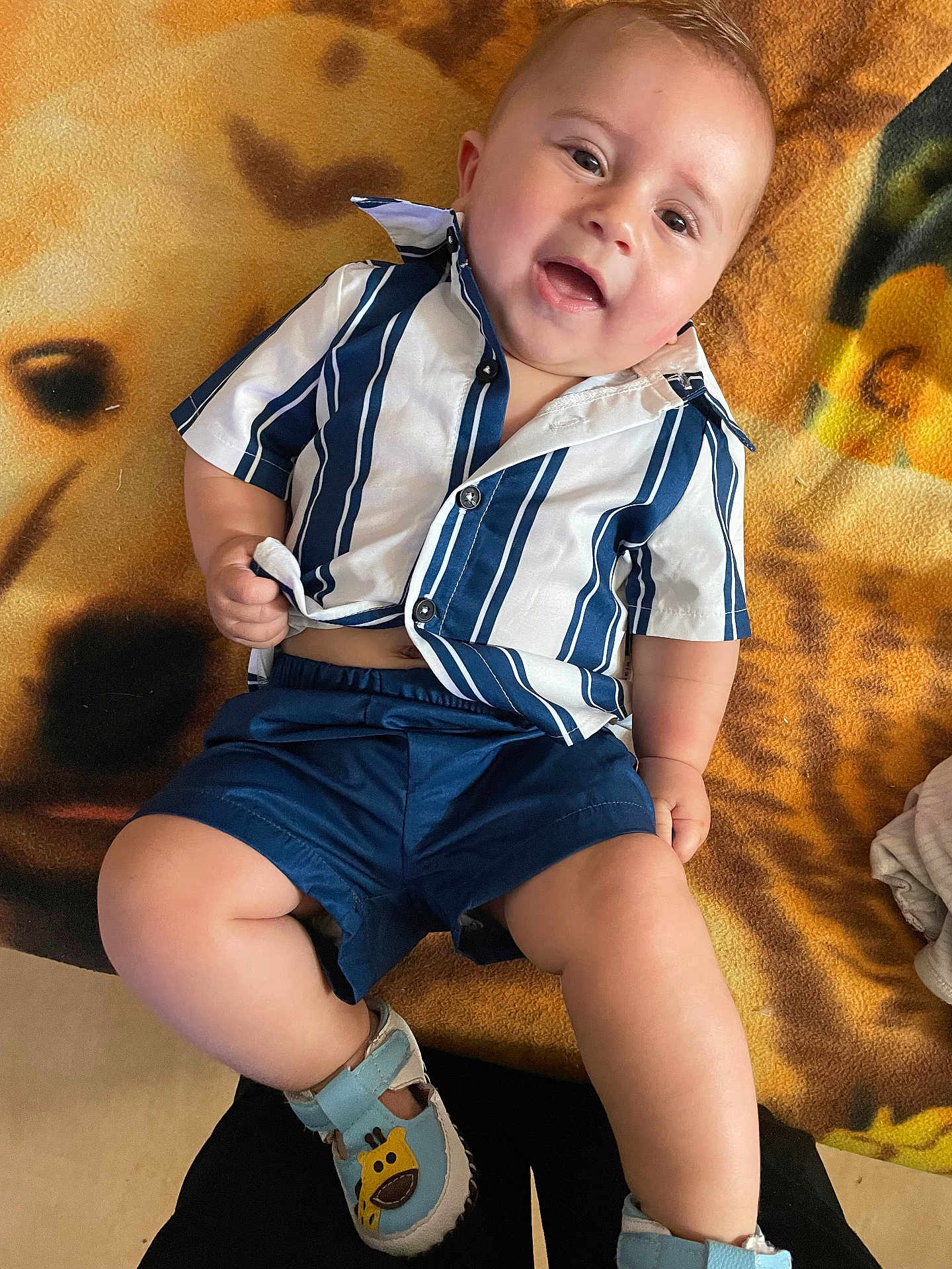 Junior participe au concours pour gagner de l'argent avec cette photo : baby, child, smiling, blue_shoes, striped_shirt, shorts, blanket, indoor, happy, cute, footwear, patterned_blanket, infant, person, young_child, casual_clothing, sitting, legs, head, face