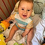 baby, child, crib, toy, smiling, happy, infant, striped_clothing, plush_toy, wooden_crib, sitting, cute, indoors, playtime, person, face, bright, colorful, fun, joyful