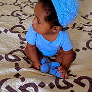 Jaden is registered to the contest to win money with this photo: baby, child, toddler, sitting, bed, bedroom, blue_outfit, knitted_hat, hat, portrait, profile, face, person, baby_socks, curly_hair, looking_sideways, indoor, bedding, patterned_blanket, photography