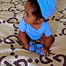 baby, child, toddler, sitting, bed, bedroom, blue_outfit, knitted_hat, hat, portrait, profile, face, person, baby_socks, curly_hair, looking_sideways, indoor, bedding, patterned_blanket, photography
