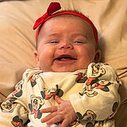 Mattie-Jean is registered to the contest to win money with this photo: baby, infant, smiling, red_headband, bow, mickey_mouse, pattern, clothing, lying_down, soft_surface, cute, happy, child, person, face, hand, apparel, indoors, portrait, cozy