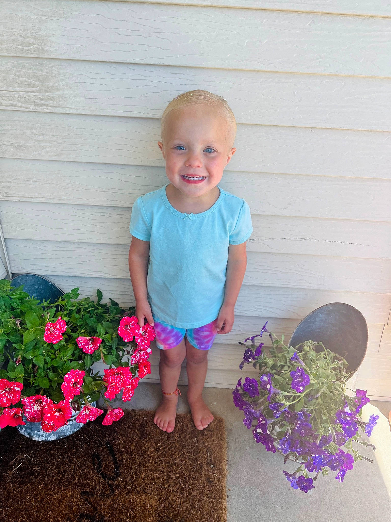 Ava is registered to the contest to win money with this photo: annual_plant, baby_toddler_clothing, electric_blue, flower, fun, garden, grass, happy, joy, leisure, magenta, pattern, people_in_nature, person, petal, pink, plant, shorts, sitting, smile