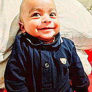 Yahya joined the competition — help win amazing prizes! baby, smiling, child, face, navy_blue_clothing, teddy_bear_emblem, pillow, indoor, happy, cute, portrait, infant, sitting, young_child, person, closeup, head, eyes, cheeks, buttoned_shirt