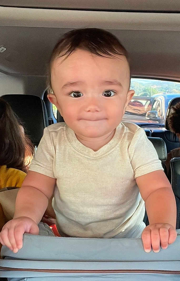 Gianni is registered to the contest to win money with this photo: toddler, child, car_interior, seat, hands, curious, portrait, person, vehicle, window, face, young_child, casual_clothing, short_sleeves, baby, grip, car_seat, looking_at_camera, smile, inside_car