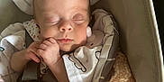 Evelyn Marie is registered to the contest to win money with this photo: baby, sleeping, blanket, knitted, carrier, face, infant, peaceful, cozy, headrest, hands, clothing, indoors, portrait, resting, young_child, cute, soft_lighting, comfort, nap