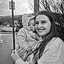 Harper is registered to the contest to win money with this photo: baby, child, young_woman, smiling, hooded_jacket, outdoor, street, sidewalk, cars, trees, urban, black_and_white, portrait, holding, people, face, clothing, weather, daytime, happy