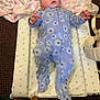 baby, infant, blue_onesie, floral_pattern, changing_pad, star_pattern, blanket, pink_blanket, carpet, footwear, boot, person, face, hands, lying_down, indoor, cute, soft_texture, child, casual