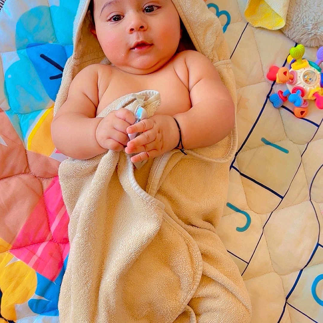 Abhik is registered to the contest to win money with this photo: baby, towel, hood, bear_ears, play_mat, toy, blanket, infant, child, cute, soft_toy, colorful, lying_down, indoors, skin, smiling, hands, feet, face, person