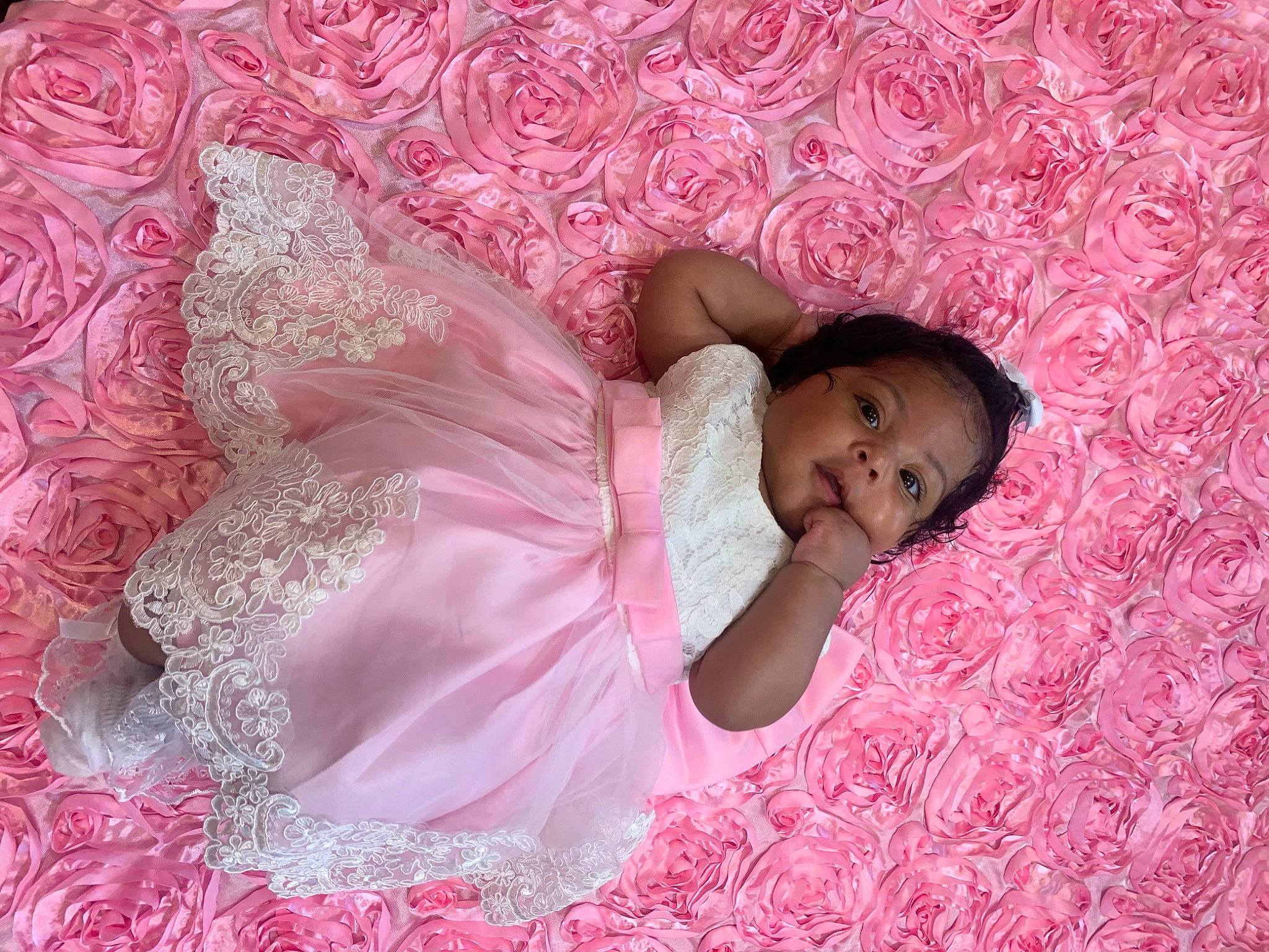 Eliana is registered to the contest to win money with this photo: arm, baby_toddler_clothing, child, comfort, dress, embellishment, eyelash, facial_expression, finger, hand, happy, leg, linens, magenta, pattern, person, petal, pink, skin, textile