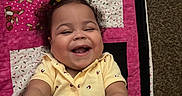 Arianna Long is registered to the contest to win money with this photo: toddler, child, smiling, laughing, yellow_clothing, curly_hair, quilt, monkey_pattern, playful, hands, carpet, indoor, happy, cute, baby, person, portrait, infant, joyful, candid