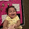 toddler, child, smiling, laughing, yellow_clothing, curly_hair, quilt, monkey_pattern, playful, hands, carpet, indoor, happy, cute, baby, person, portrait, infant, joyful, candid