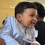 Leo is registered to the contest to win money with this photo: toddler, child, smiling, white_clothing, embroidery, indoors, furniture, happy, portrait, curly_hair, person, modern_lighting, cute, baby, laughing, hand, face, head, people, background