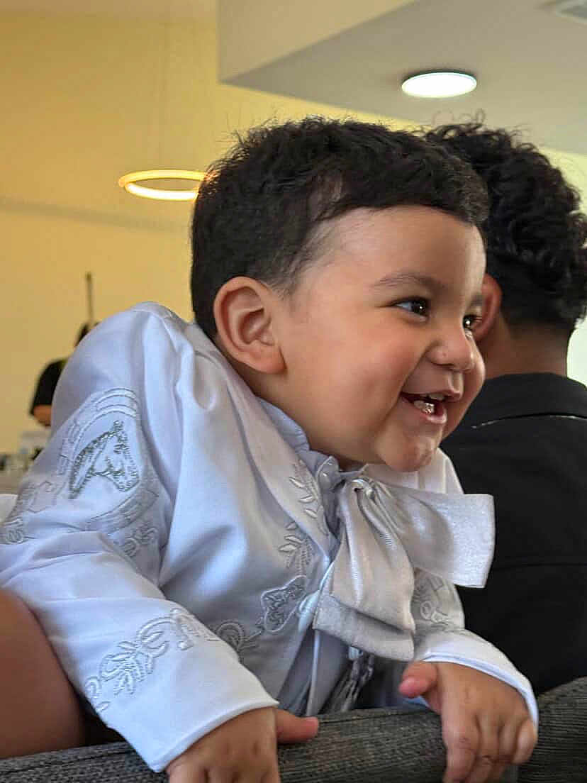 Leo is registered to the contest to win money with this photo: toddler, child, smiling, white_clothing, embroidery, indoors, furniture, happy, portrait, curly_hair, person, modern_lighting, cute, baby, laughing, hand, face, head, people, background