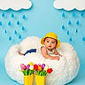 baby, yellow_hat, fluffy_cushion, clouds, raindrops, blue_background, yellow_rain_boots, tulips, colorful_flowers, indoor, child, cute, spring_theme, playful, portrait, smiling, decor, flower_arrangement, childrens_photography, studio_shot
