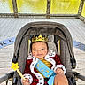 baby, child, crown, star_wand, red_robe, blue_sash, stroller, smile, outdoor, deck, wooden_floor, fence, water, greenery, portrait, cute, happy, costume, person, infant
